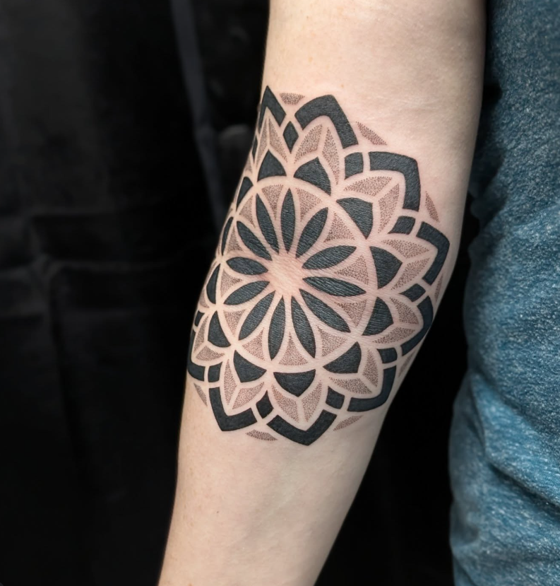Black and gray geometric mandala tattoo on an elbow with dotwork shading